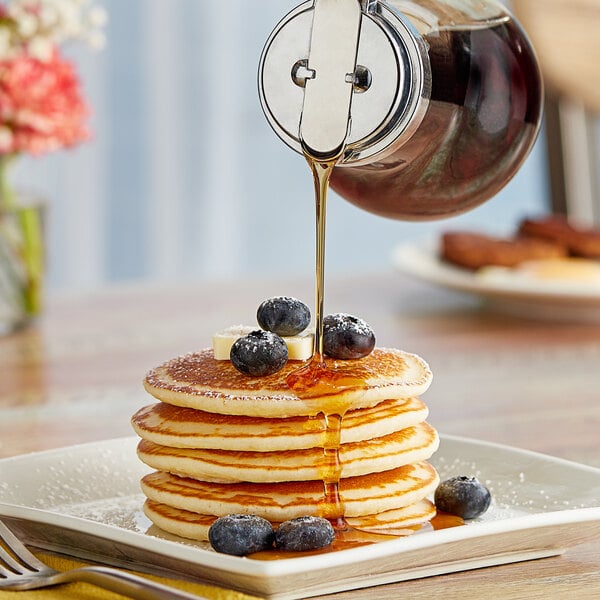 A stack of pancakes with Log Cabin syrup being poured over them.