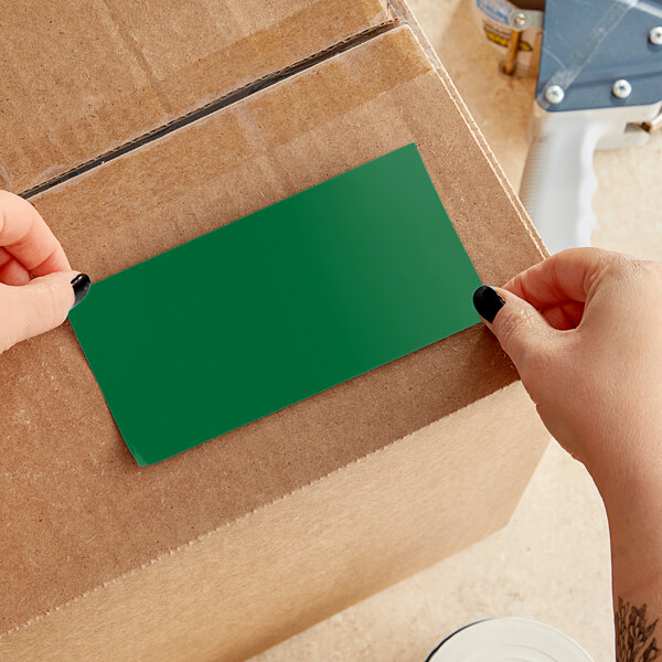 A person using a blue and white handled cutter to cut a green rectangular paper.