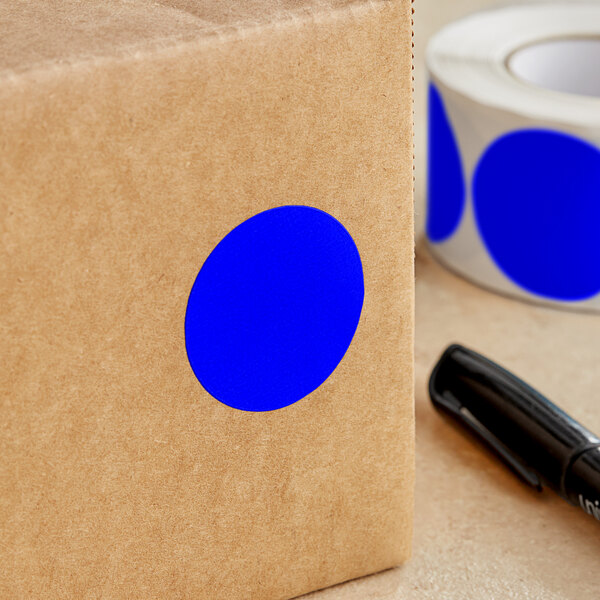 A brown box with a blue circle sticker next to a roll of tape.