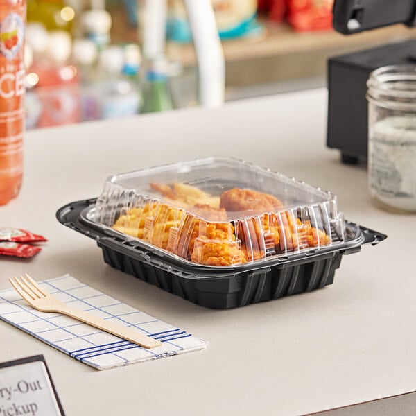 A Pactiv black plastic container of chicken barns on a table.