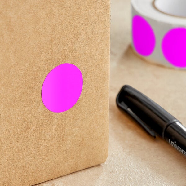 A roll of Lavex pink round inventory labels with a pink oval label on brown paper with a black pen.