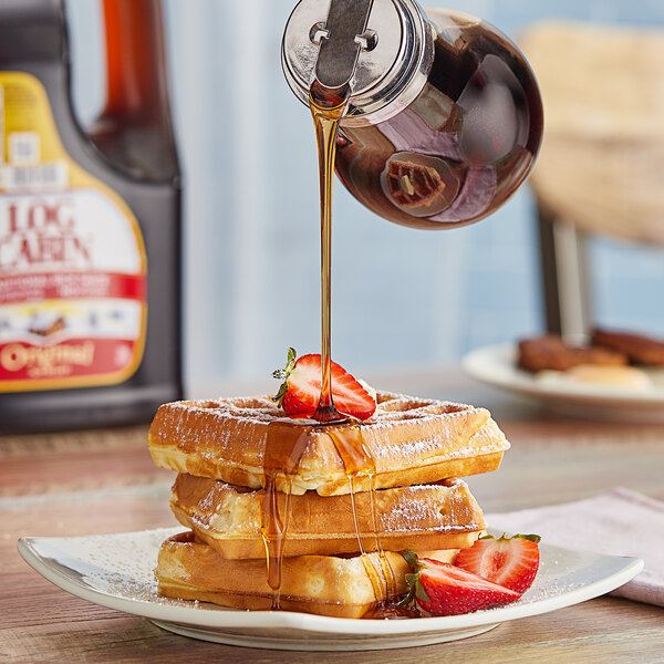 A person pouring Log Cabin Original syrup onto a stack of waffles on a table.
