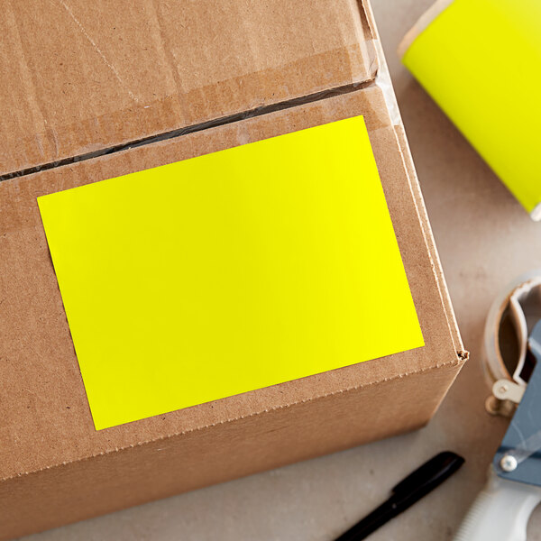 A roll of Lavex bright yellow rectangular inventory labels with a yellow sticker on a cardboard box.