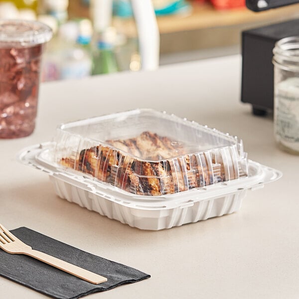 A Pactiv white plastic chicken barn filled with food on a black surface.