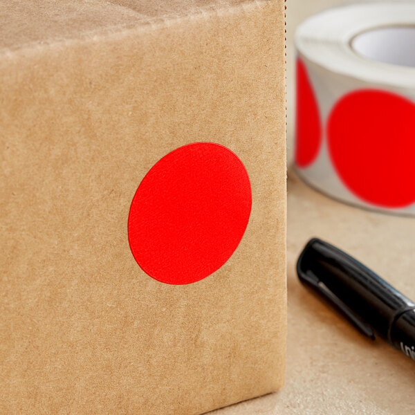 A brown box with a roll of Lavex fluorescent red inventory labels with a red dot on it next to a black pen.