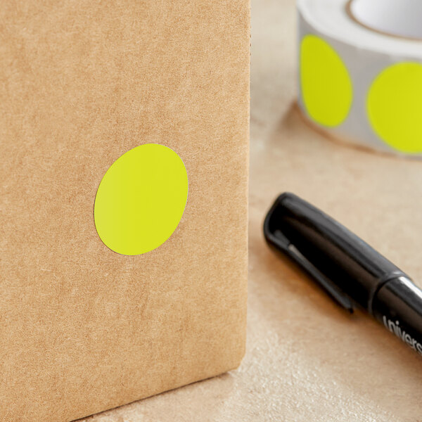 A roll of Lavex fluorescent chartreuse round inventory labels with a yellow oval label on a brown surface next to a black marker.