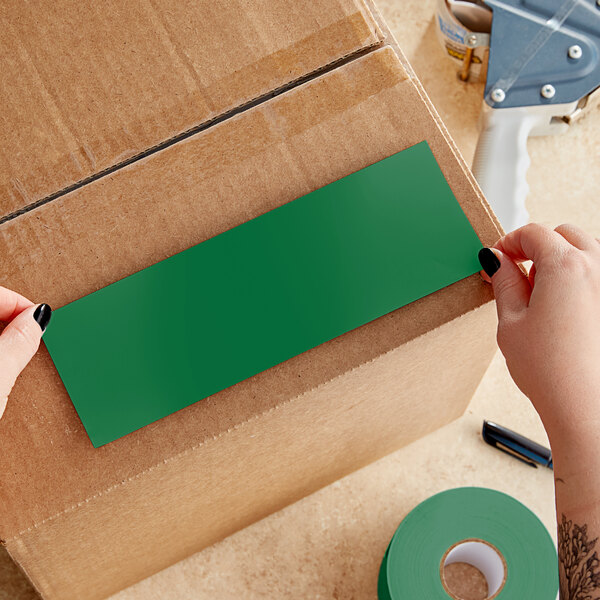 A person's hands applying a green rectangular Lavex inventory label to a box.