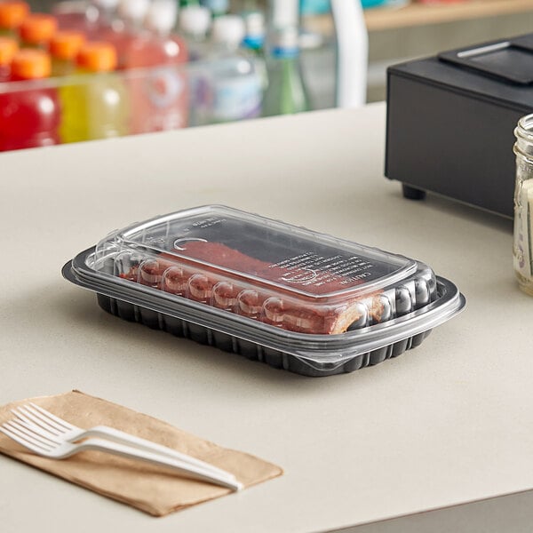 A Pactiv plastic container with sausages in it on a deli counter.