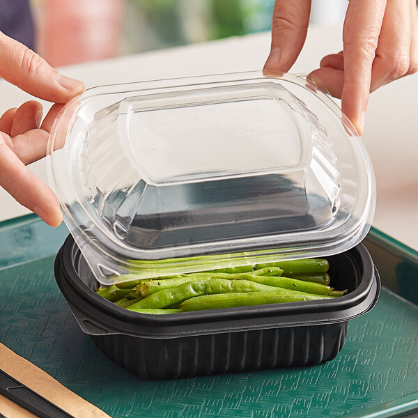 A person holding a Pactiv plastic container with green beans in it.