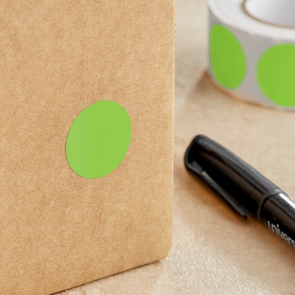 A roll of Lavex fluorescent green round inventory labels with white and green stickers on a brown surface next to a black pen.