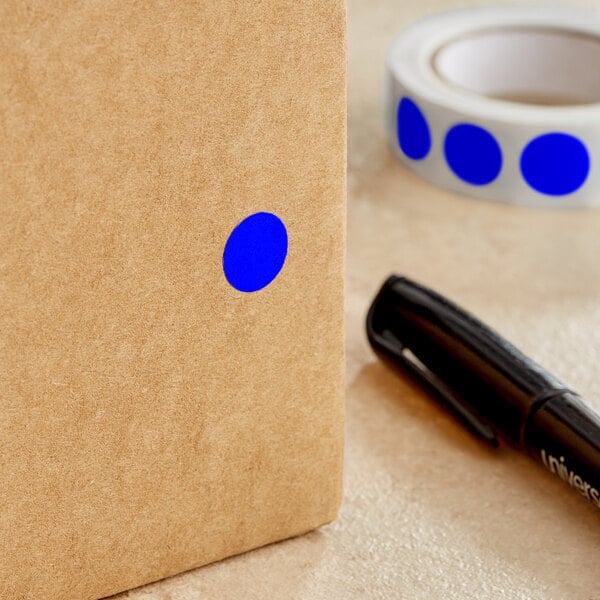 A roll of Lavex dark blue round inventory labels with a semi-gloss finish with a blue dot on a brown surface next to a black pen.