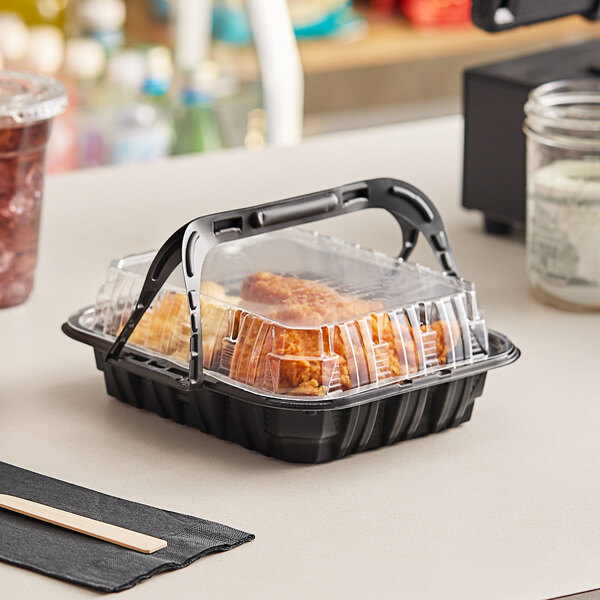 A Pactiv black plastic MealMaster chicken barn with food inside on a counter.