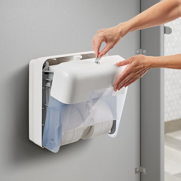 A person's hand opening a white Tork OptiServe coreless toilet paper dispenser.