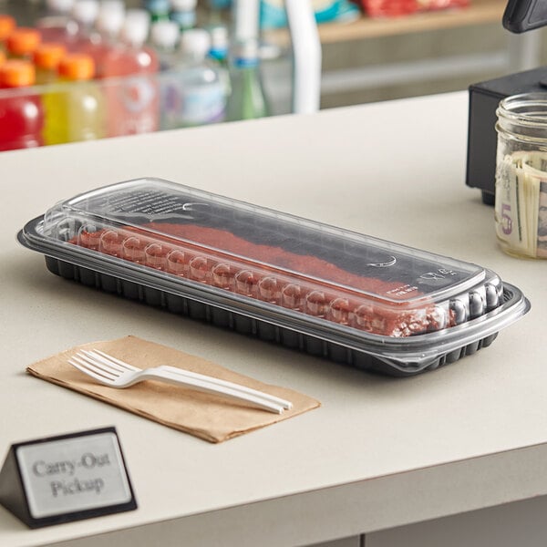 A Pactiv black plastic container filled with ribs on a table.