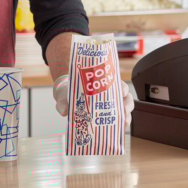 A person holding a Bagcraft clown popcorn bag full of popcorn.