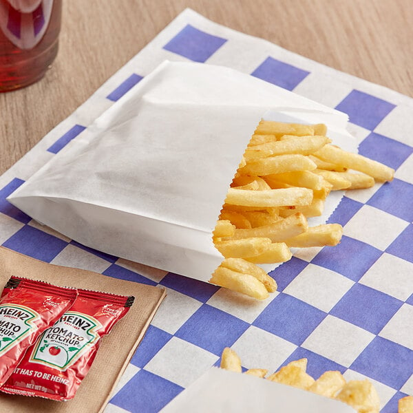 A bag of Bagcraft white french fries on a checkered table with ketchup packets.