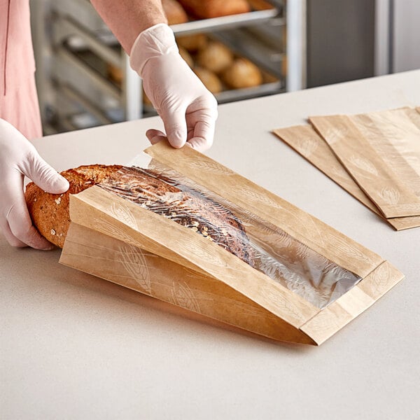 A person in gloves putting a loaf of bread into a Bagcraft natural artisan print bread bag.