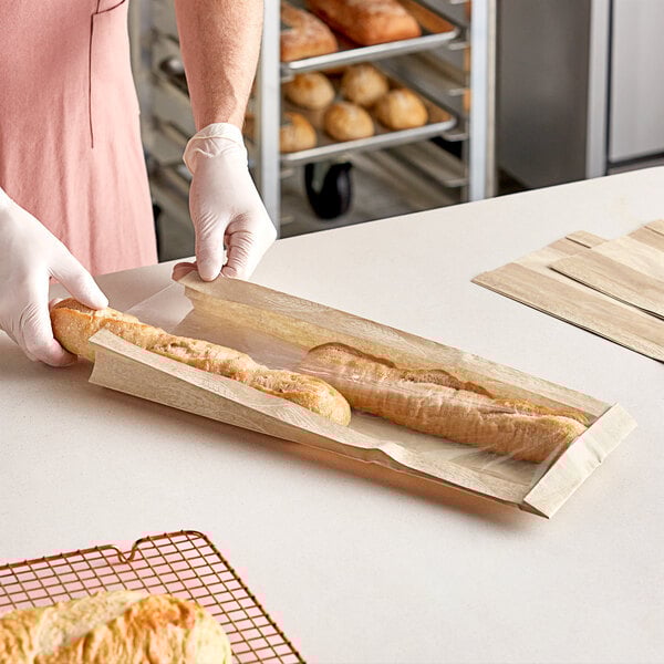 A person in gloves is cutting a baguette in a Bagcraft Natural Artisan Print bread bag.