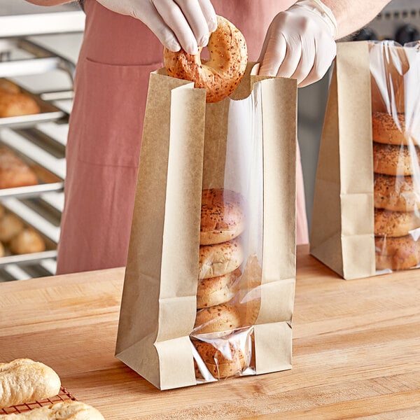 A person putting bagels into a Bagcraft natural bakery bag with a window.