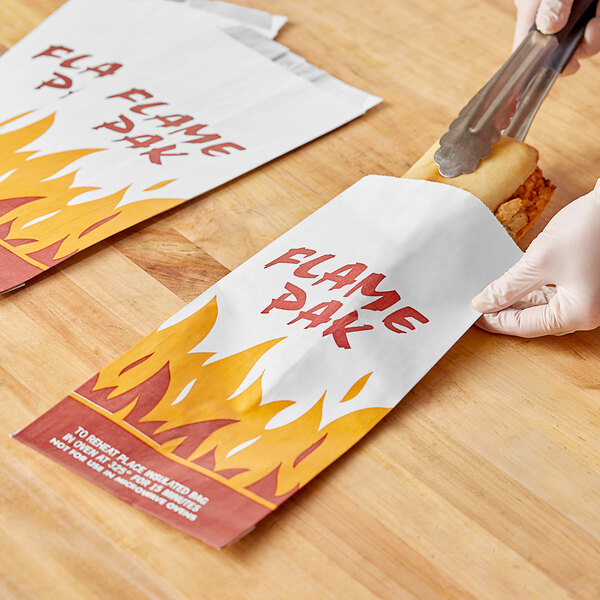 A person using a knife to cut a Bagcraft Flame Pak meal bag filled with hot dogs.