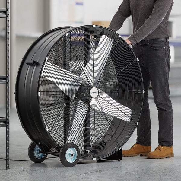 A man standing next to a large black Boltic portable direct-drive drum fan on wheels.