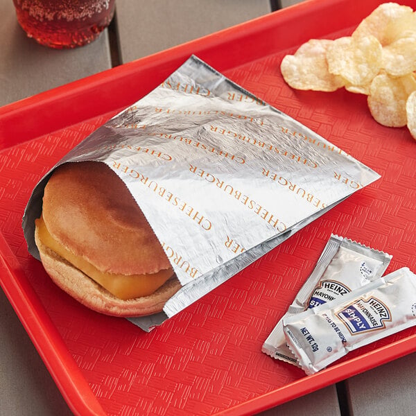 A cheeseburger and chips in a Bagcraft foil wrapper on a red tray.