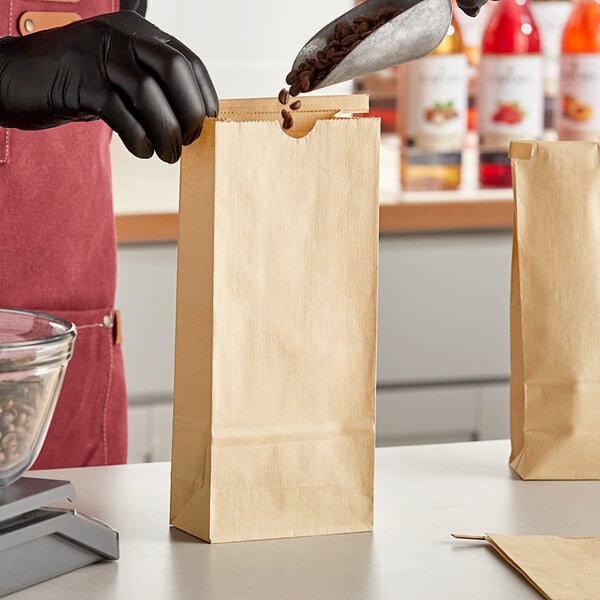 A person using a scoop to pour coffee beans into a Bagcraft natural kraft coffee bag.