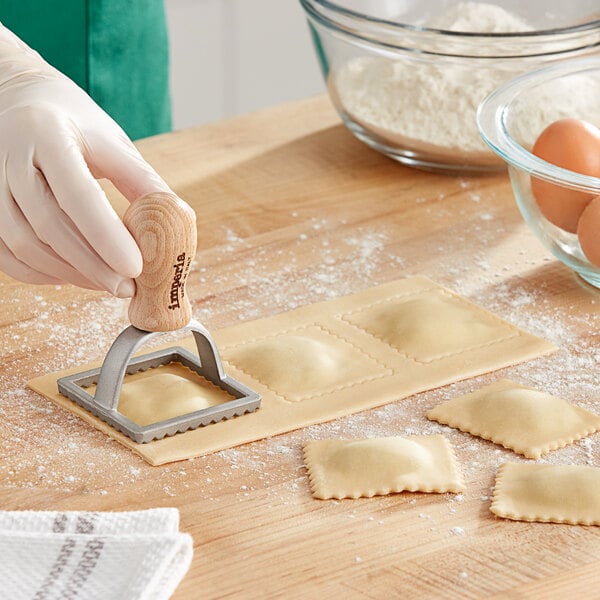 A person using an Imperia square ravioli stamp to cut pasta.