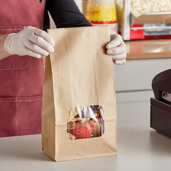 A person in gloves holding a Bagcraft natural tortilla chip bag with food inside.
