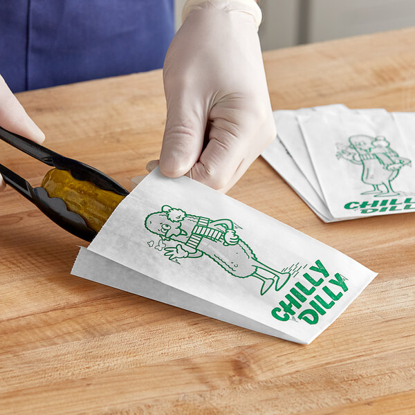 A person's gloved hand holding a Bagcraft dry wax pickle bag with a pickle inside.