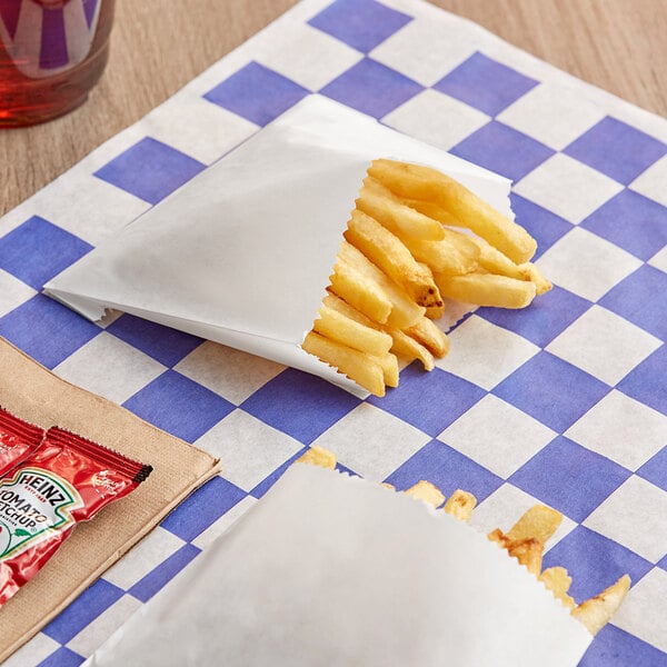 French fries in a Bagcraft white paper bag on a checkered table.