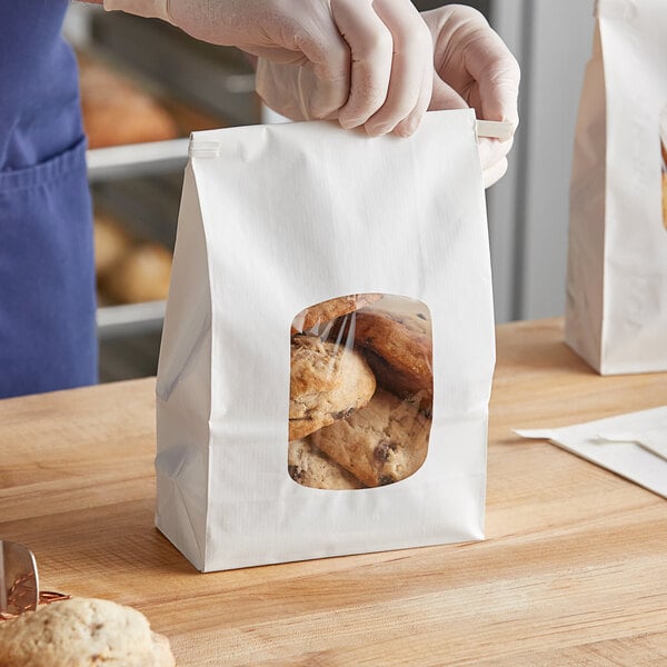 A person holding a Bagcraft white stand-up bakery bag with cookies inside.