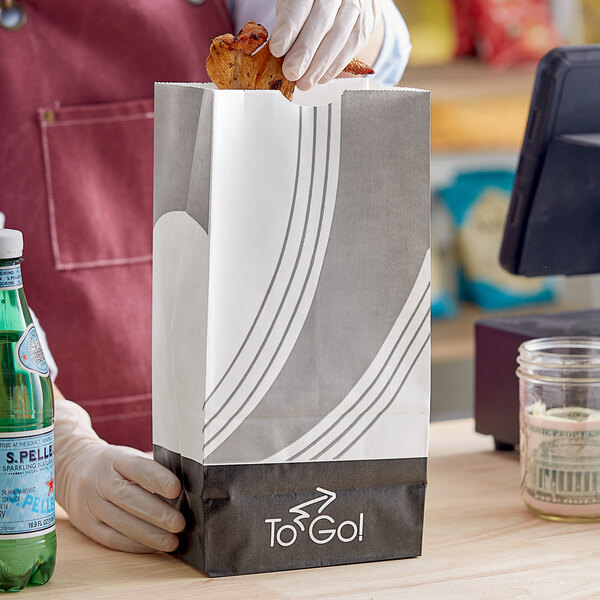 A gloved hand holding a white Bagcraft meal bag full of food.