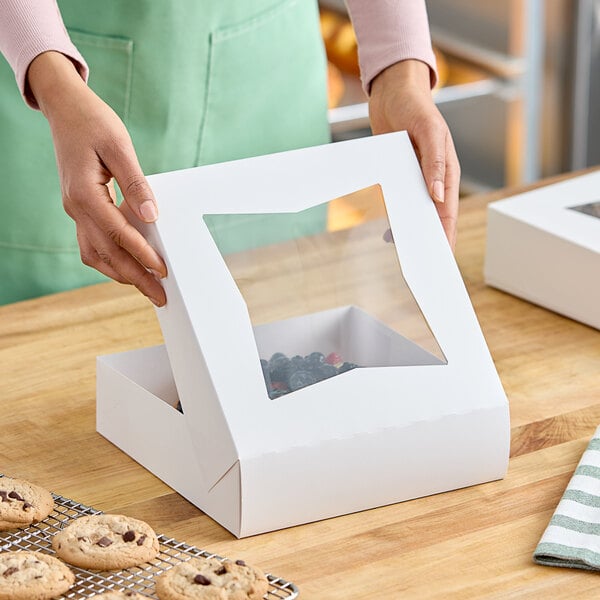 A woman holding a white Baker's Lane pie box with a clear window.