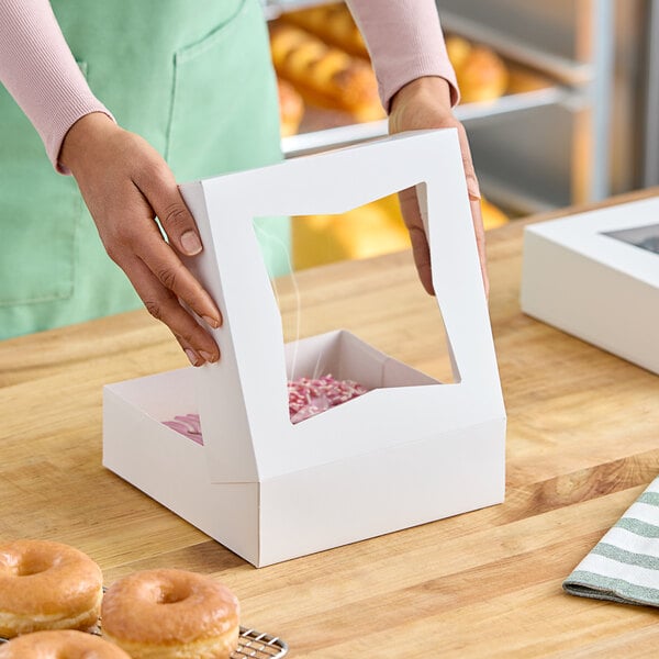 A person holding a white Baker's Lane pie box with a window.