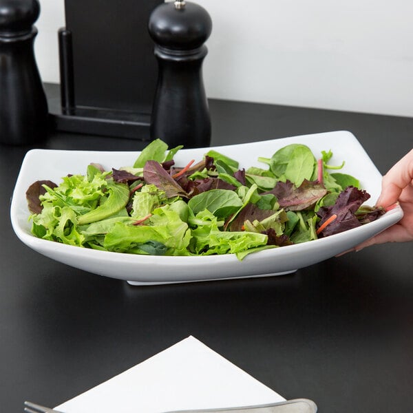 A person holding an American Metalcraft oval stoneware bowl of salad.