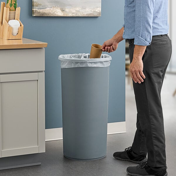 A man standing next to a Lavex Gray round wastebasket in a corporate cafeteria.