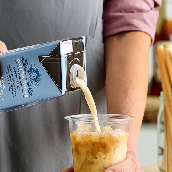 A person pouring Califia Farms Barista Blend Oat Milk into a cup of coffee.