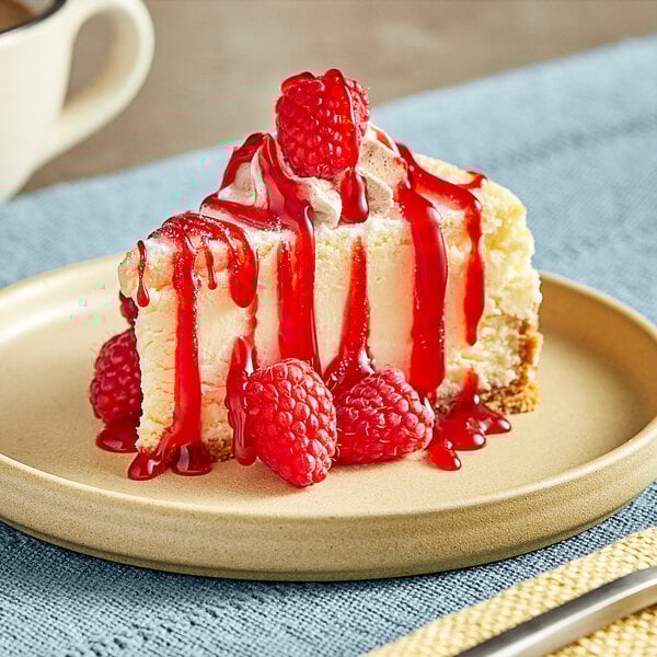 A slice of cheesecake with raspberries and Lyons raspberry sauce on a plate.