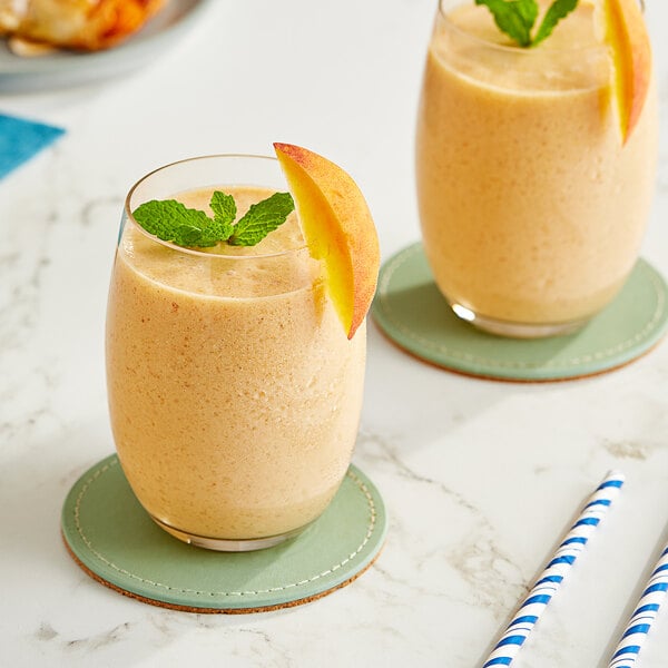 Two glasses of Maui by Lyons peach smoothie with fruit slices and a mint leaf on top.