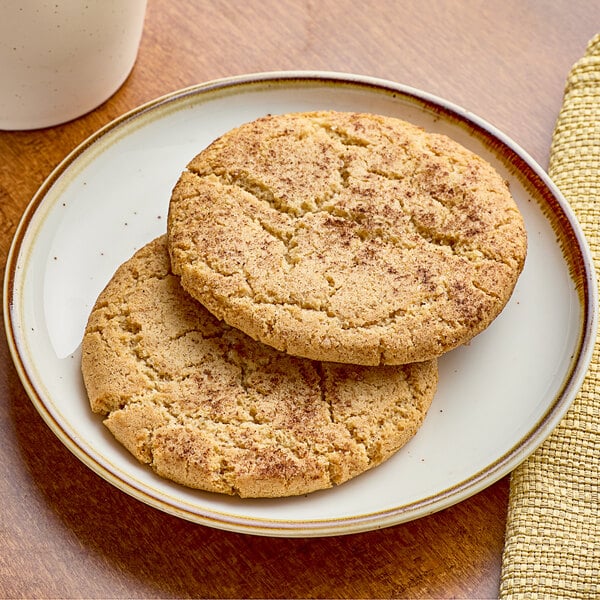 Two Red Plate Foods Individually Wrapped Vegan Snickerdoodle cookies on a plate next to a white cup of coffee.