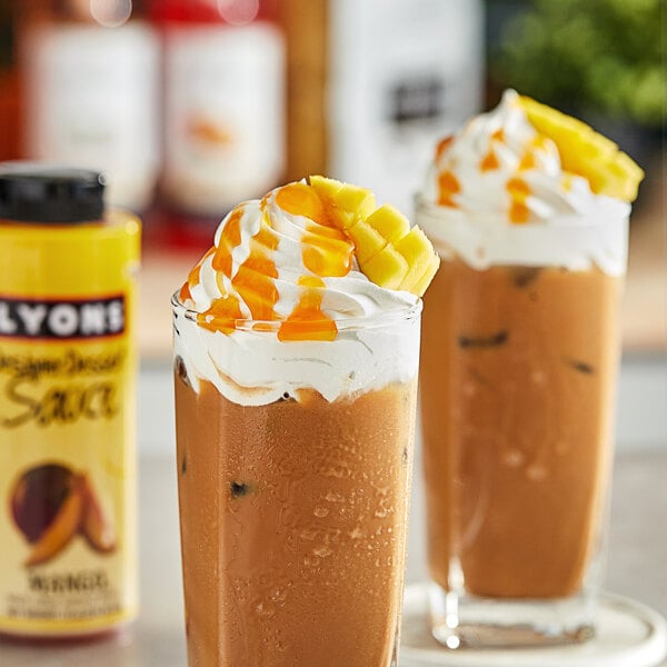 Two glasses of iced coffee with whipped cream and yellow mango sauce on a table.