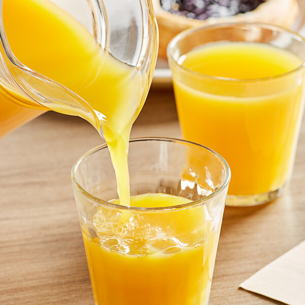 A glass of Ocean Spray Orange Juice being poured from a glass pitcher.