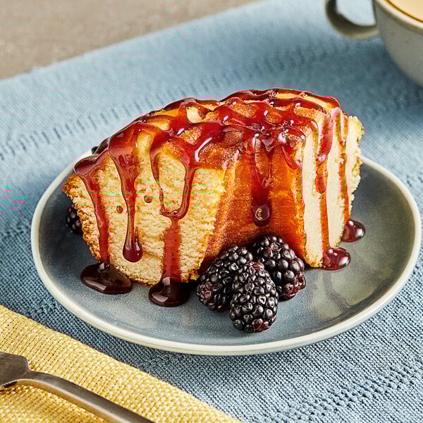 A piece of cake with Lyons Blackberry Flavoring Sauce and berries on a plate.