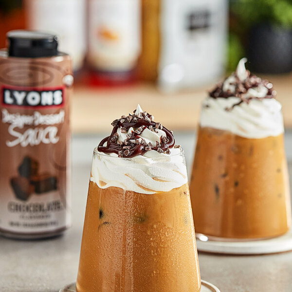 Two glasses of chocolate pudding topped with Lyons chocolate sauce on a counter.