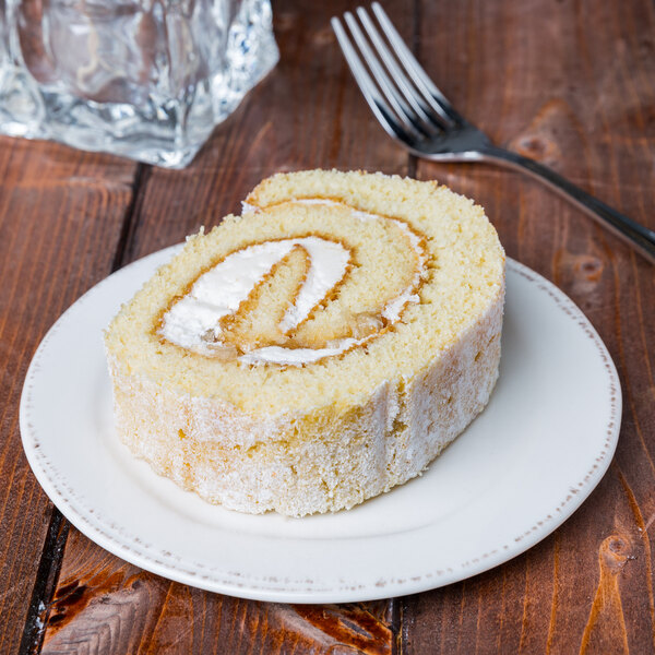 A slice of rolled sponge cake with cream filling on a round cream-colored porcelain plate.