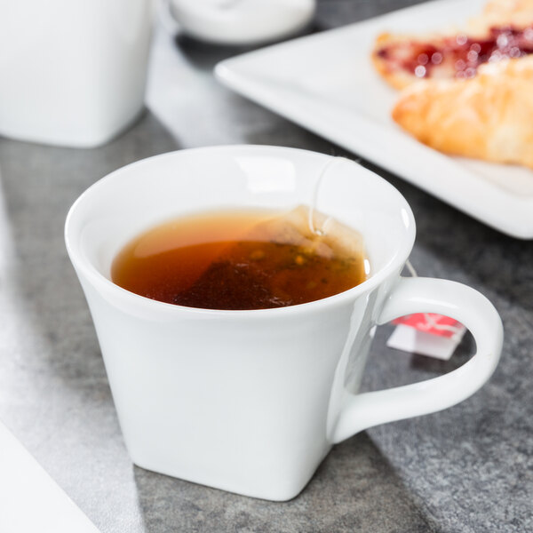 A close up of a Libbey Slate Ultra Bright White porcelain cup filled with tea on a table.