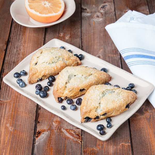 A rectangular cream porcelain tray displaying three blueberry scones, surrounded by fresh blueberries.