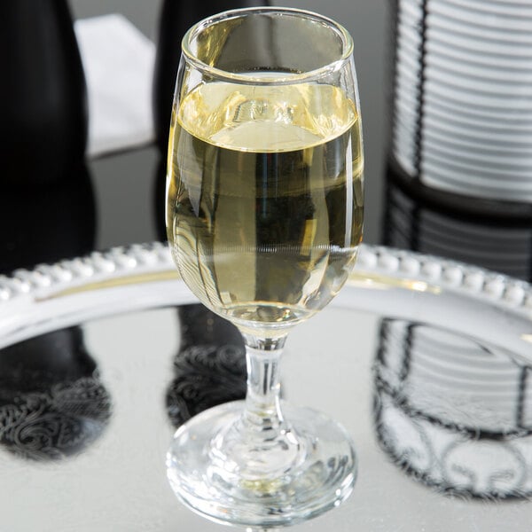 A Libbey white wine glass filled with yellow liquid on a silver tray.