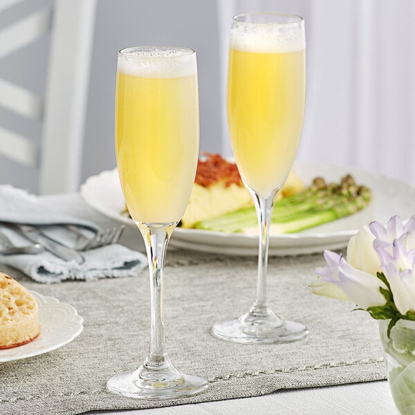 Two Libbey Embassy Tall Flute glasses filled with yellow liquid on a table.